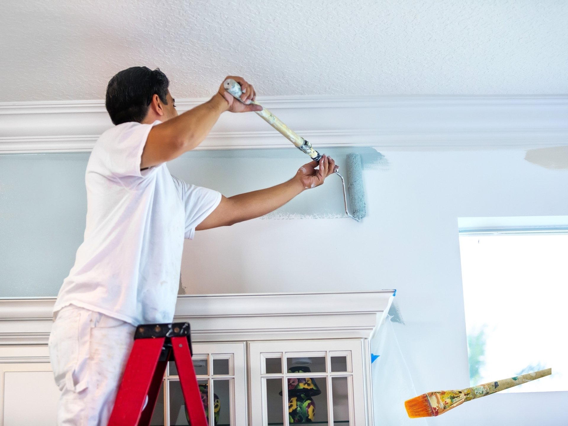 Interior house painter on a ladder applying blue paint to a living room wall with precision and care.